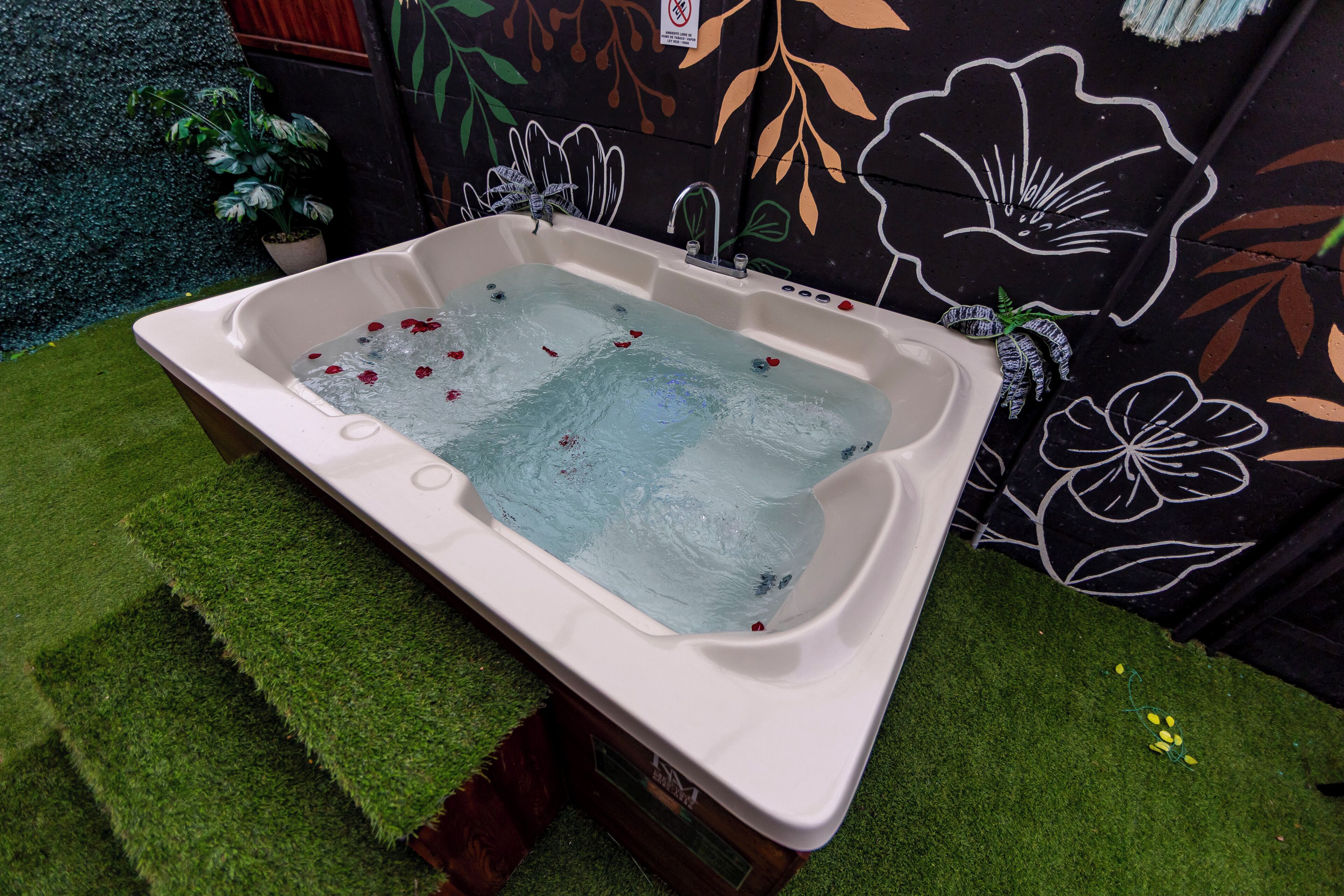 A bathtub with water, surrounded by artificial grass and a wall with floral patterns.