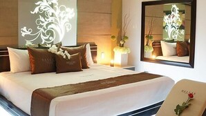Moderni hotellihuone, jossa on suuri sänky, yöpöytä, peili ja koristeellinen seinäpaneeli.