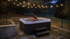 Un bain à remous avec des marches, entouré d’un jardin et illuminé de guirlandes lumineuses.
