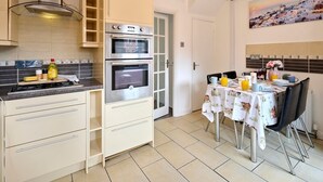 A kitchen with two ovens, a stove, and a dining area with a table set for two. - Home in Milton Keynes (Great Holm)