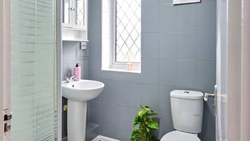 A bathroom with a glass shower enclosure, a pedestal sink, a toilet, and a window with a decorative item.