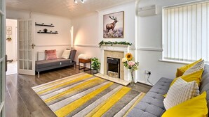 A living room with a fireplace, a sofa, a striped rug, and a deer painting on the wall. - Home in Milton Keynes (Great Holm)