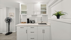 A modern kitchen with white cabinets, a sink, a fan, and a potted plant.