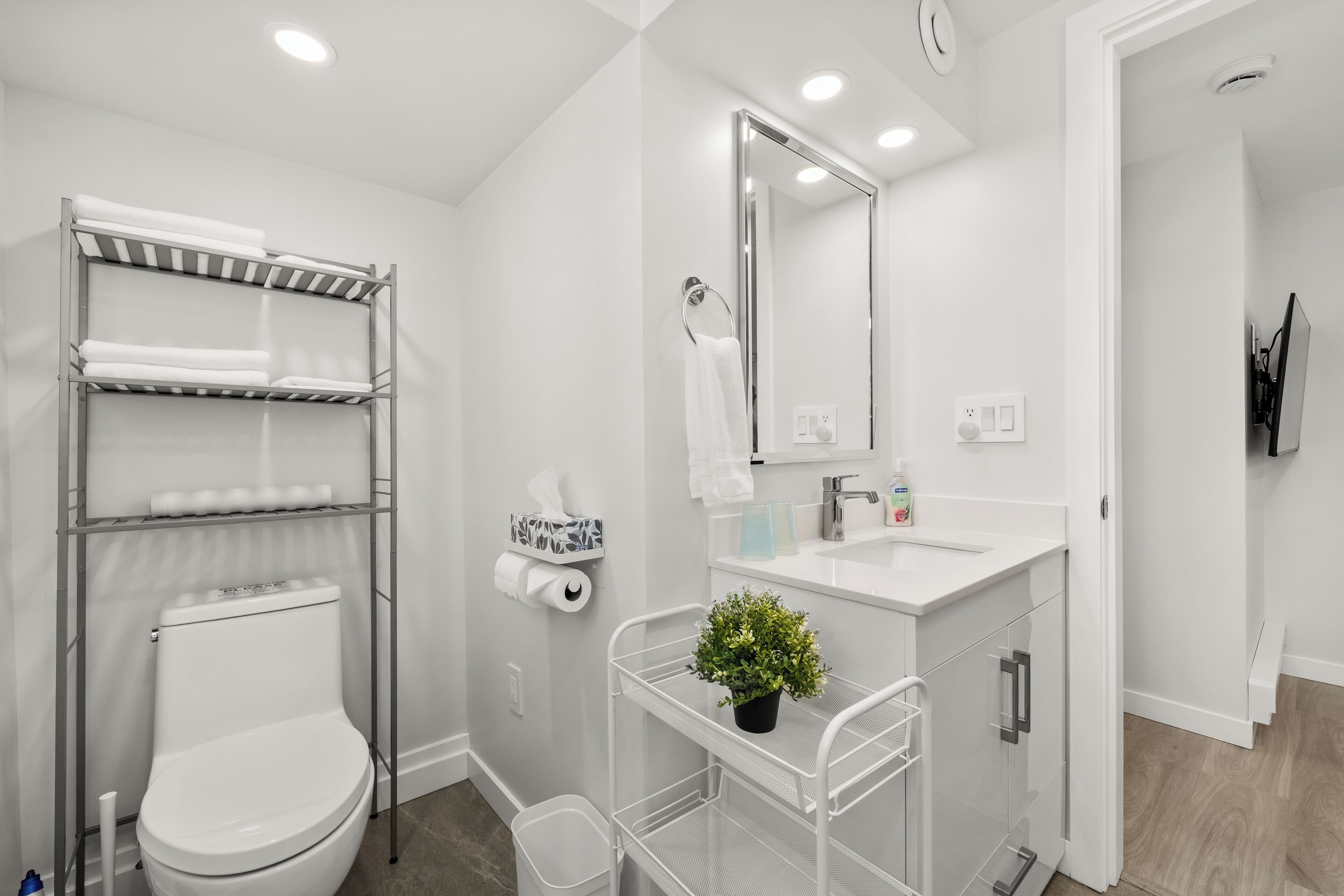 A modern bathroom with a toilet, shelves, a sink, a mirror, and a potted plant.