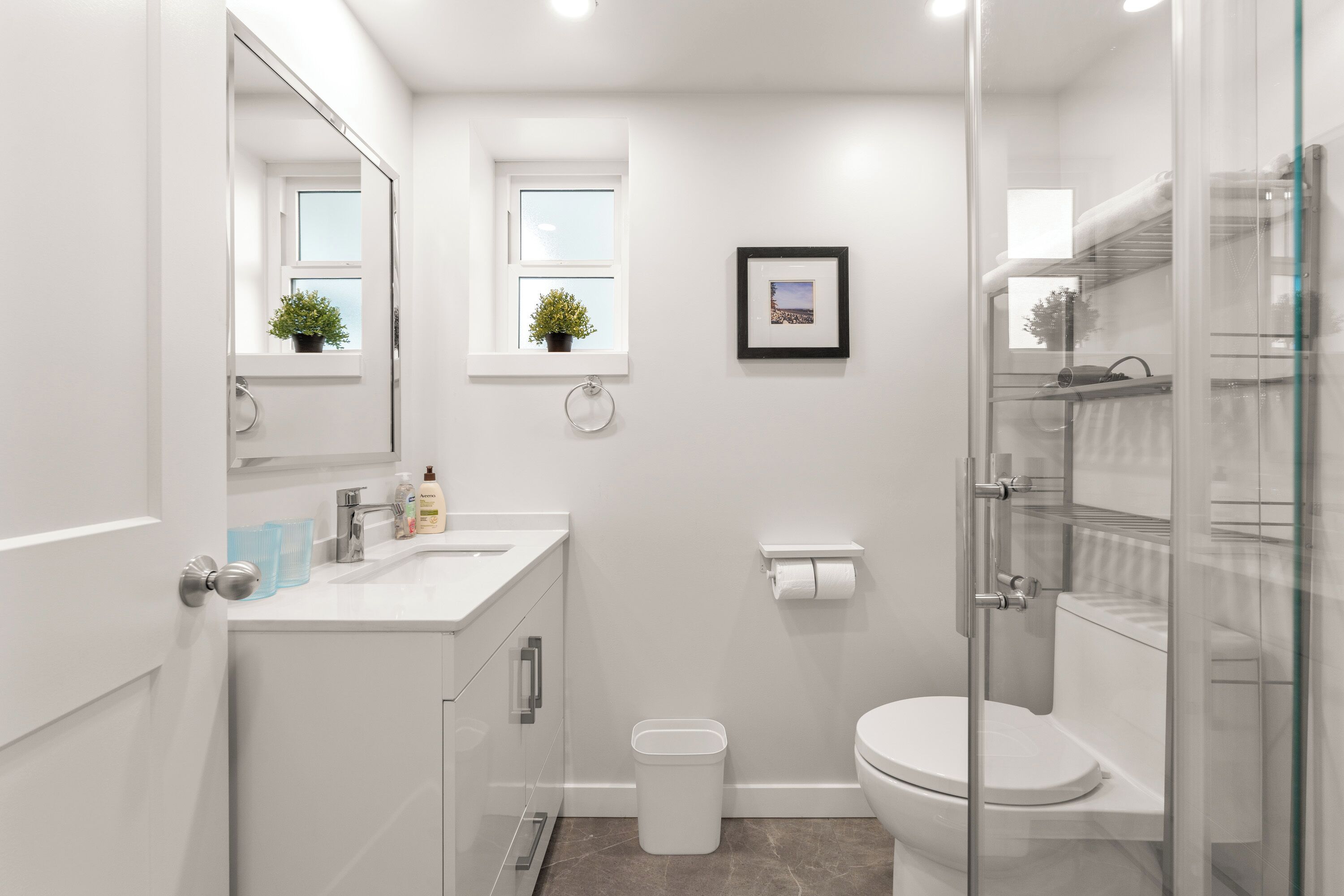 Un bany modern amb plat de dutxa de vidre, un lavabo blanc amb mirall i un vàter.