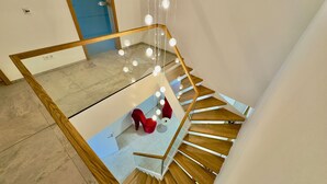 A modern staircase with wooden steps and glass railings, leading to a mezzanine with a red chair and a hanging light fixture.