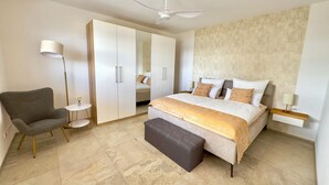 A bedroom with a bed, a chair, a wardrobe, a mirror, and a ceiling fan.