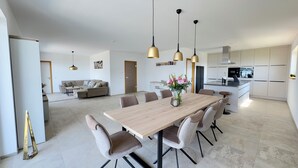 A modern kitchen with white cabinets and a central island, a dining area with a wooden table and chairs, and a living area with a sofa and a coffee table.
