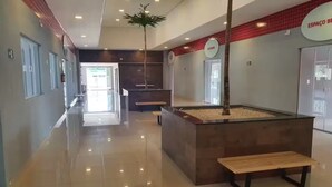 Um hall moderno com piso lustroso, balcão de recepção, um banco e uma planta decorativa.