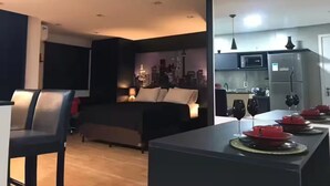 Uma sala de estar moderna com um mural da paisagem urbana, uma área de refeições com pratos vermelhos e uma cozinha com geladeira e micro-ondas.
