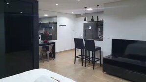 Uma sala de estar moderna com sofá, TV e um espaço de jantar com cadeiras e mesa.