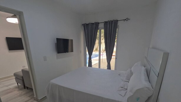 Ein Hotelzimmer mit Bett, Fernseher, Fenster mit Vorhängen und Blick auf einen Pool.