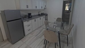 Eine moderne Küche mit weißen Schränken, einem Kühlschrank, einer Mikrowelle und einem Herd. Ein Glastisch mit Stühlen steht daneben.