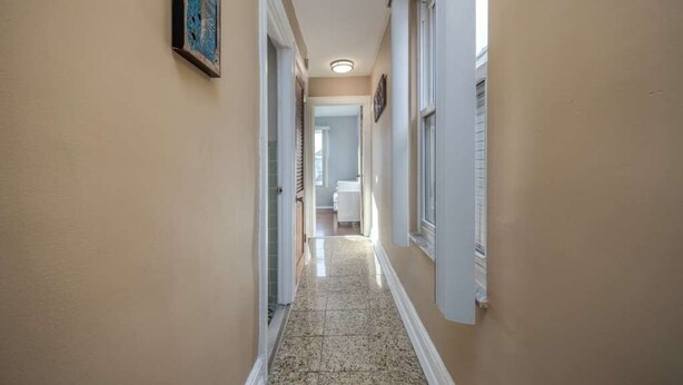 A narrow hallway with beige walls and a tiled floor, leading to a bathroom with a toilet and sink. - Chic 2-bedroom apartment (Brooklyn)