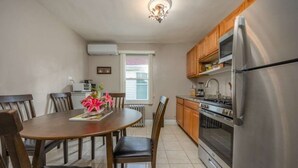 A compact kitchen with a dining table, chairs, a refrigerator, an oven, and wooden cabinets. - Chic 2-bedroom apartment (Brooklyn)