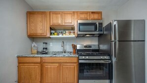 A modern kitchen with wooden cabinets, a stainless steel refrigerator, a microwave, and an oven. - Chic 2-bedroom apartment (Brooklyn)