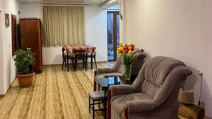 Une pièce spacieuse avec un plancher en bois, un canapé en cuir marron, une table à manger avec des chaises, une plante en pot et un vase rempli de fleurs.