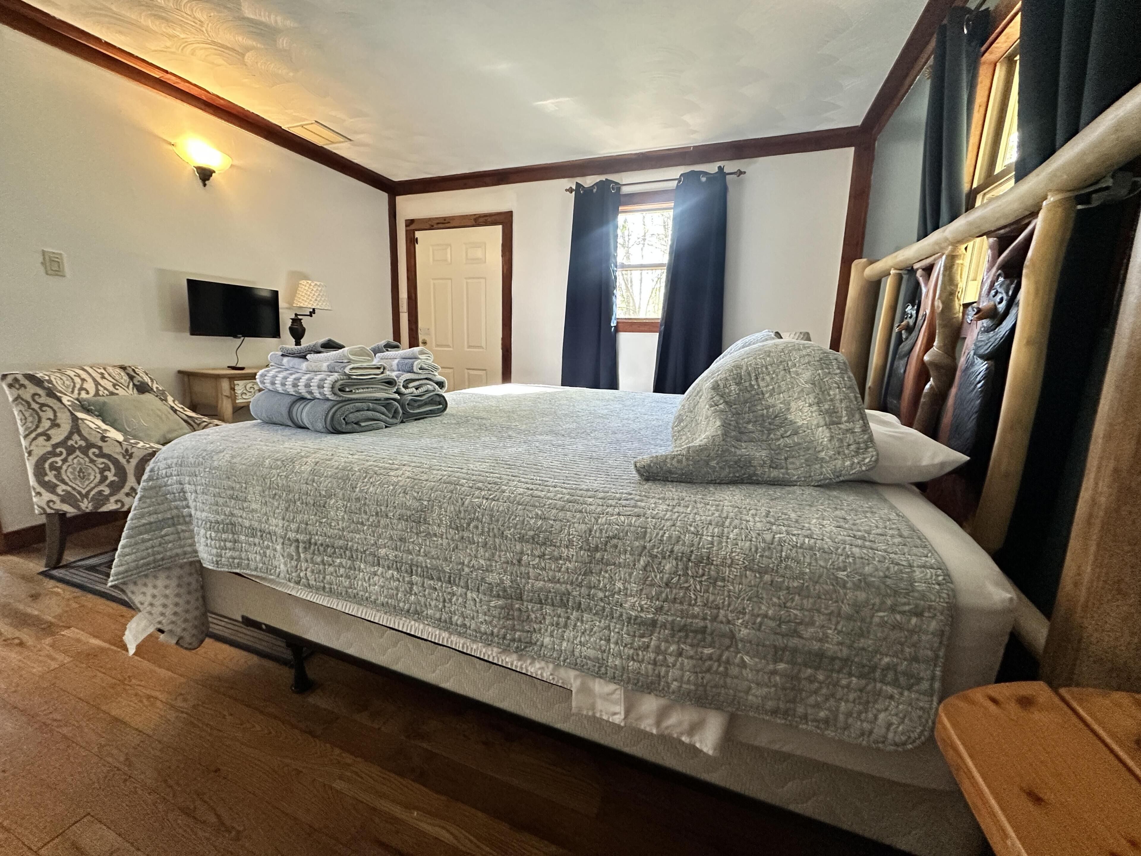 Une chambre à coucher avec un lit, une chaise, un téléviseur et une fenêtre avec des rideaux.