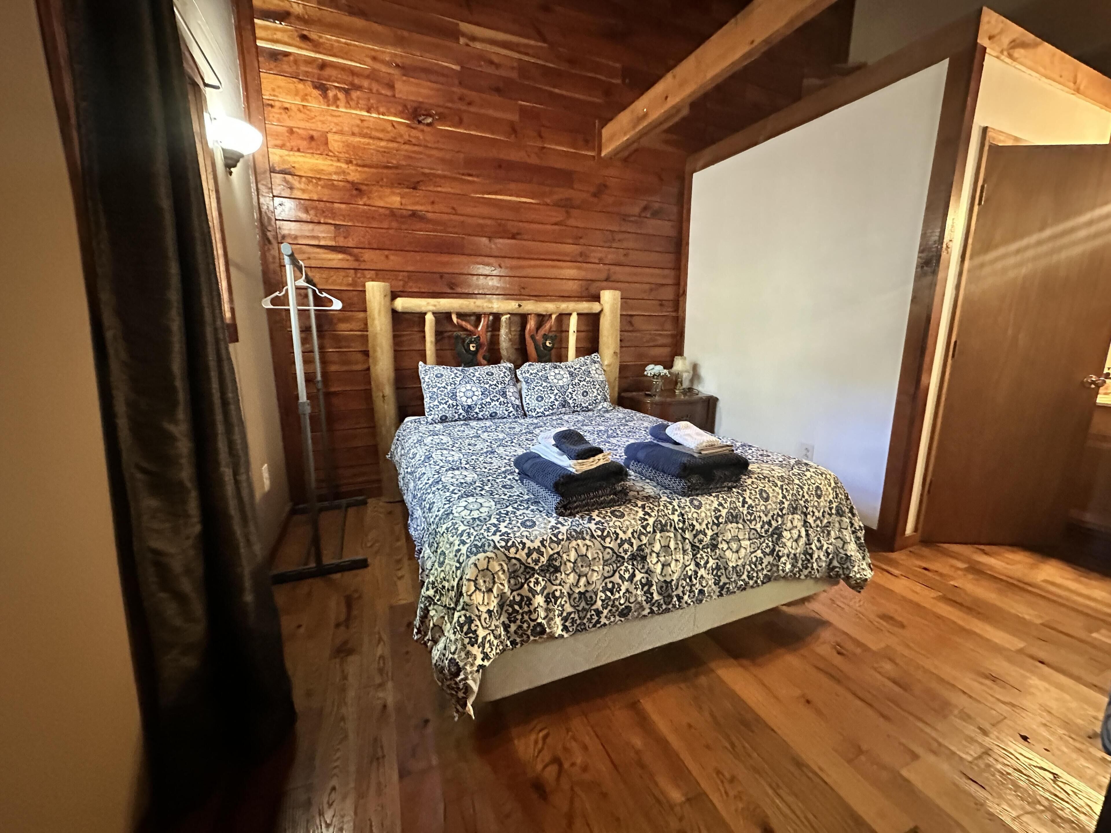 Ein Zimmer mit Holzwänden, einem Bett, einem Nachttisch und einer Tür.