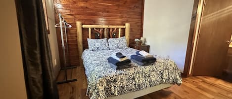 A wooden-paneled room with a bed, a nightstand, and a door.