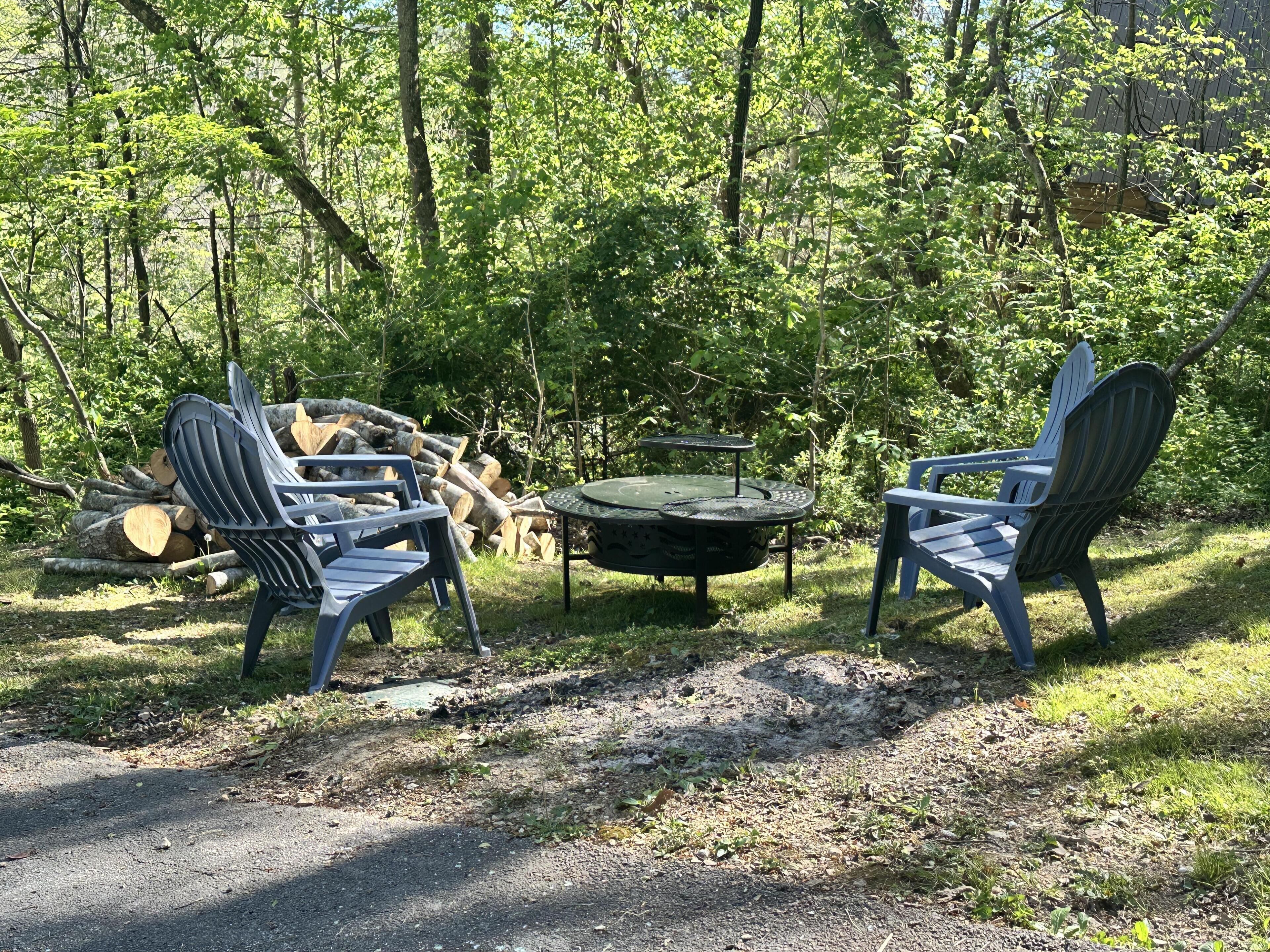 Ein Sitzbereich im Freien mit Adirondack-Stühlen und einem runden Tisch, umgeben von einem Wald.