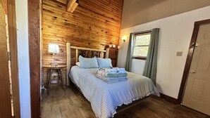 A wooden-paneled room with a bed, a nightstand, a lamp, and a window with curtains.