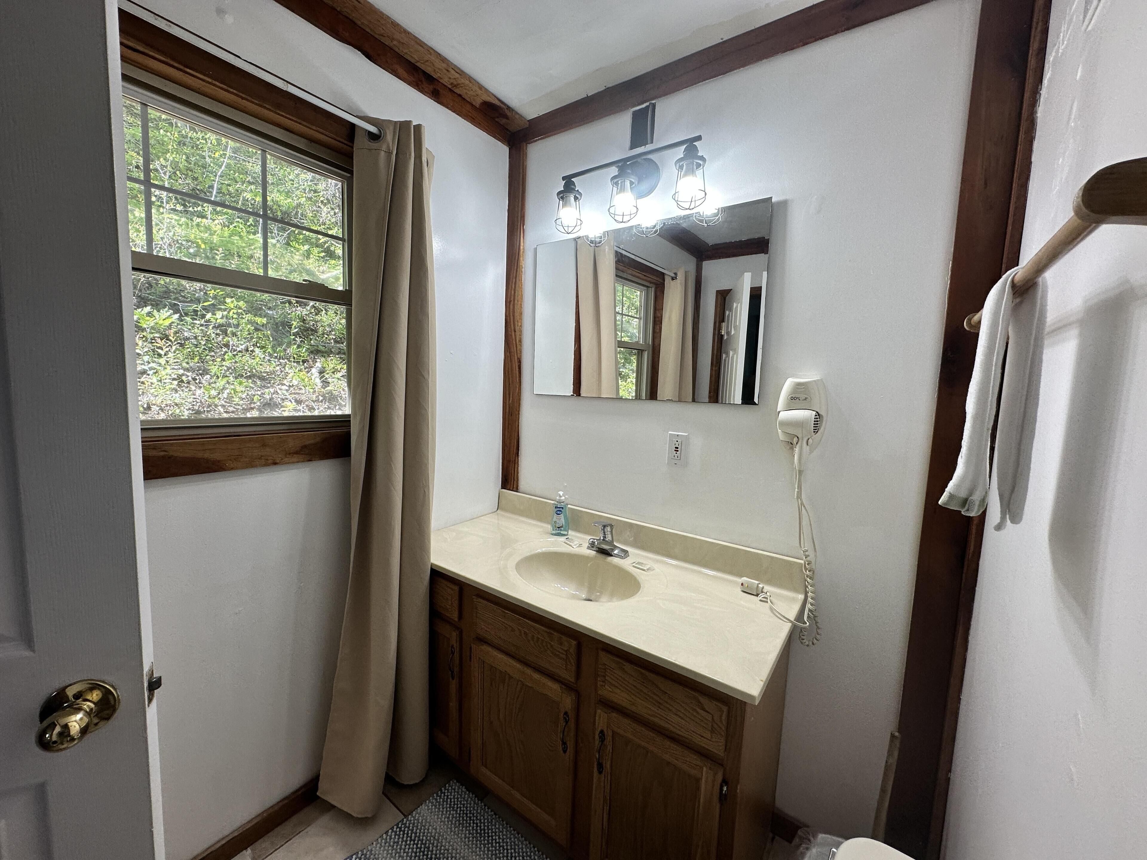 A bathroom with a window, a sink, a mirror, and a hairdryer.