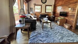 A cozy living room with a wooden ceiling, a sofa, a coffee table, and a TV on the wall.