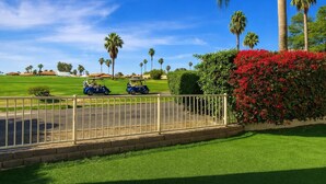 A golf course with two golf carts, palm trees, and a hedge with red flowers. - Private Pool and Spa and Cooling Misting System (Palm Desert)
