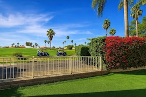 A golf course with two golf carts, palm trees, and a hedge with red flowers. - Escape to Paradise 3 bed-3 bath- Private Pool and Hot Tub Cooling Misting System (Palm Desert)