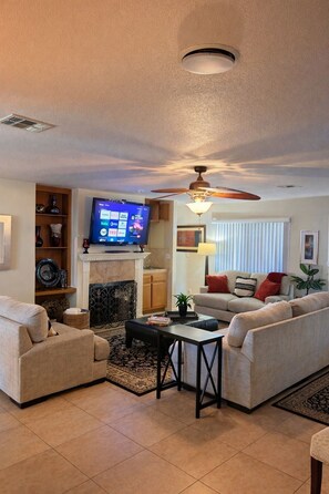 A living room with a fireplace, television, ceiling fan, and two sofas.