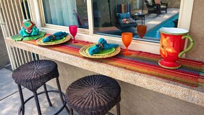 A bar area with wicker stools, a colorful woven mat, and a large decorative pitcher. - Private Pool and Spa and Cooling Misting System (Palm Desert)