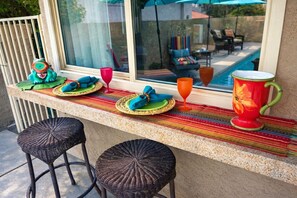 A bar area with wicker stools, a colorful woven mat, and a large decorative pitcher.