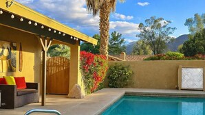 A pool area with a palm tree, a covered seating area, and a mountain view. - Private Pool and Spa and Cooling Misting System (Palm Desert)