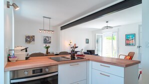 A modern kitchen with a wooden countertop, built-in oven, and white cabinets. There is a dining area with a table and chairs, and a view of the outdoors through a large window.