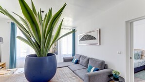 Una sala de estar moderna con una maceta azul grande con una planta, un sofá gris con cojines azules, una mesa de centro de madera y un cuadro en la pared.