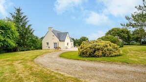 A house with a gravel driveway leading to a wooden bench.