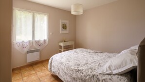A bedroom with a bed, a nightstand, a window with curtains, a wall-mounted air conditioner, and a ceiling light.