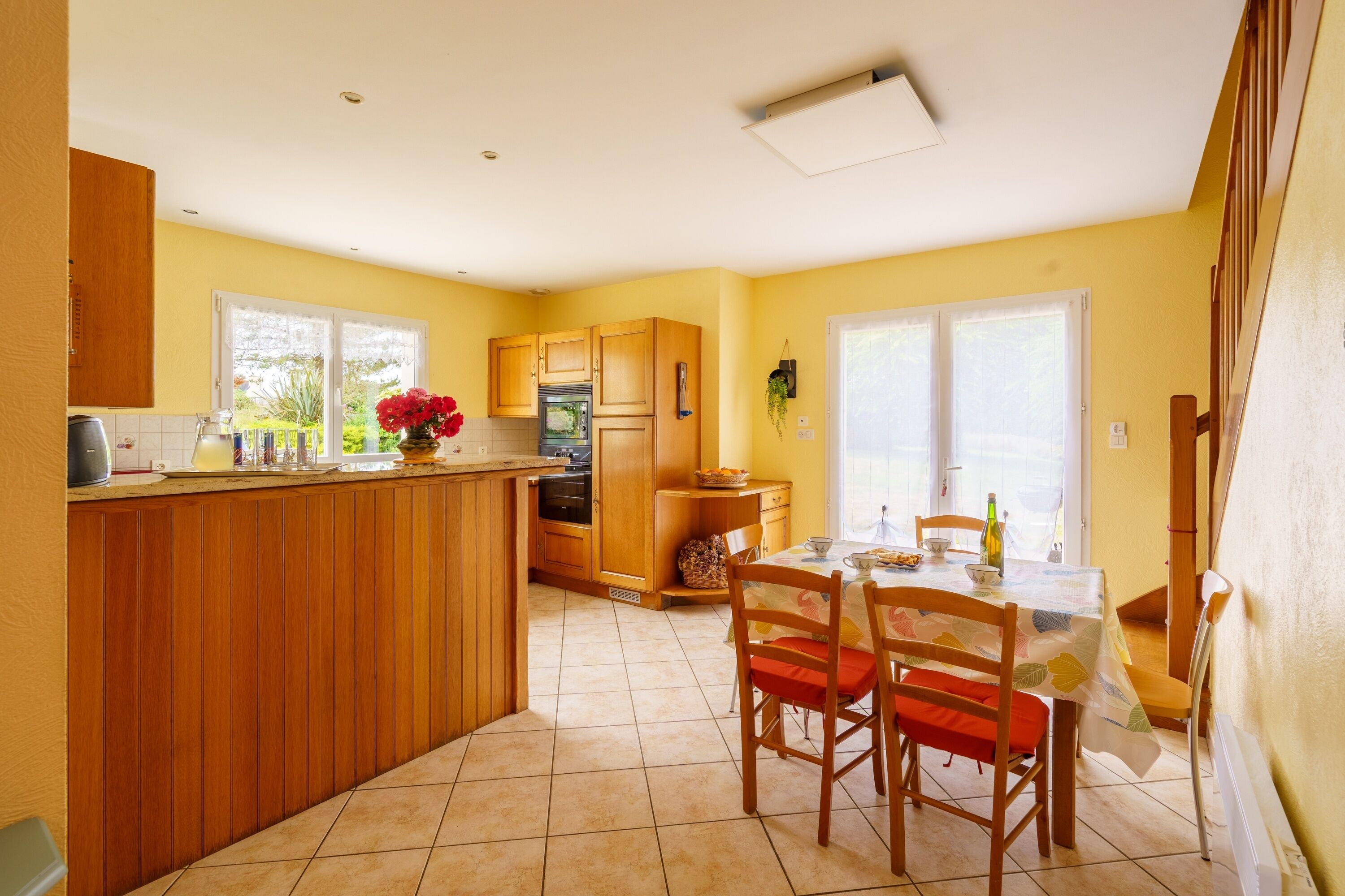 Une cuisine avec des meubles en bois, une table à manger avec des chaises et une fenêtre donnant sur un paysage verdoyant.