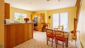 A kitchen with wooden cabinets, a dining table with chairs, and a window with a view of greenery.