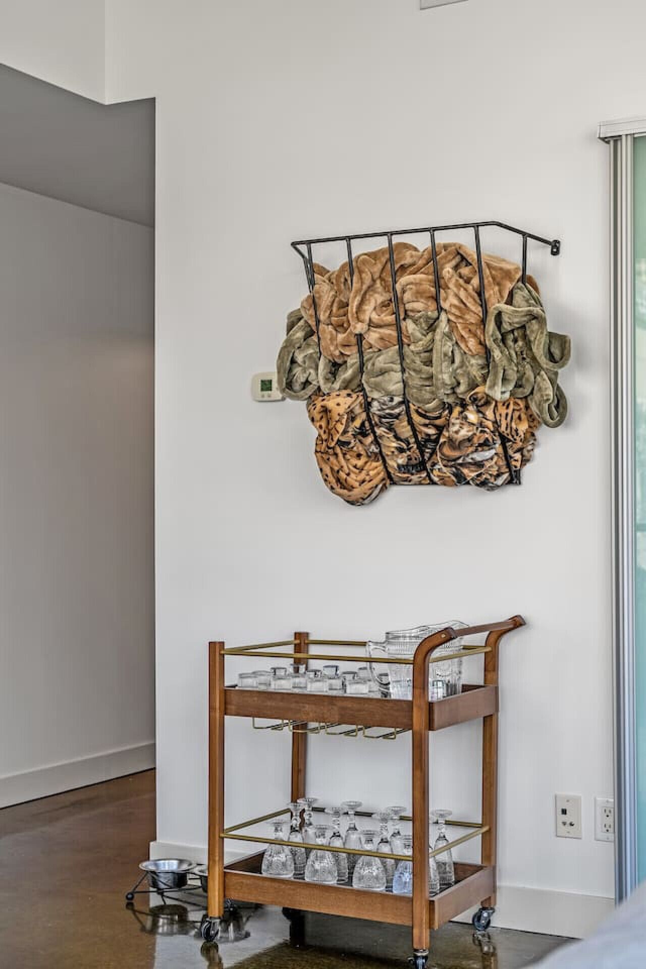 A wall-mounted rack with folded blankets and a wooden cart with glassware.