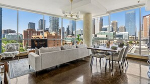 A spacious living area with a large window offering a city view, a dining table, and a sofa.