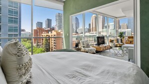 A modern bedroom with a large bed, a city view, a television, and a seating area with a coffee table.