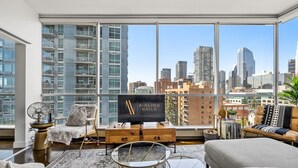 A modern living room with large windows, a flat-screen TV, and a city view.
