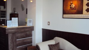 A reception desk with a wooden finish, a framed artwork above it, and a white sofa with a brown pillow in the foreground. - Hotel Sol (Mar del Plata)
