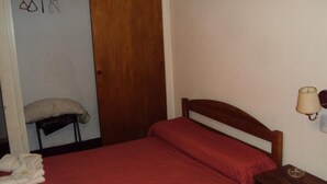 A bedroom with a wooden bed, a red mattress, a wooden nightstand with a lamp, and a chair with a cushion. - Hotel Sol (Mar del Plata)