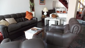 A living room with a sofa, armchair, and coffee table. There is a dining area with a table and chairs in the background. - Hotel Sol (Mar del Plata)