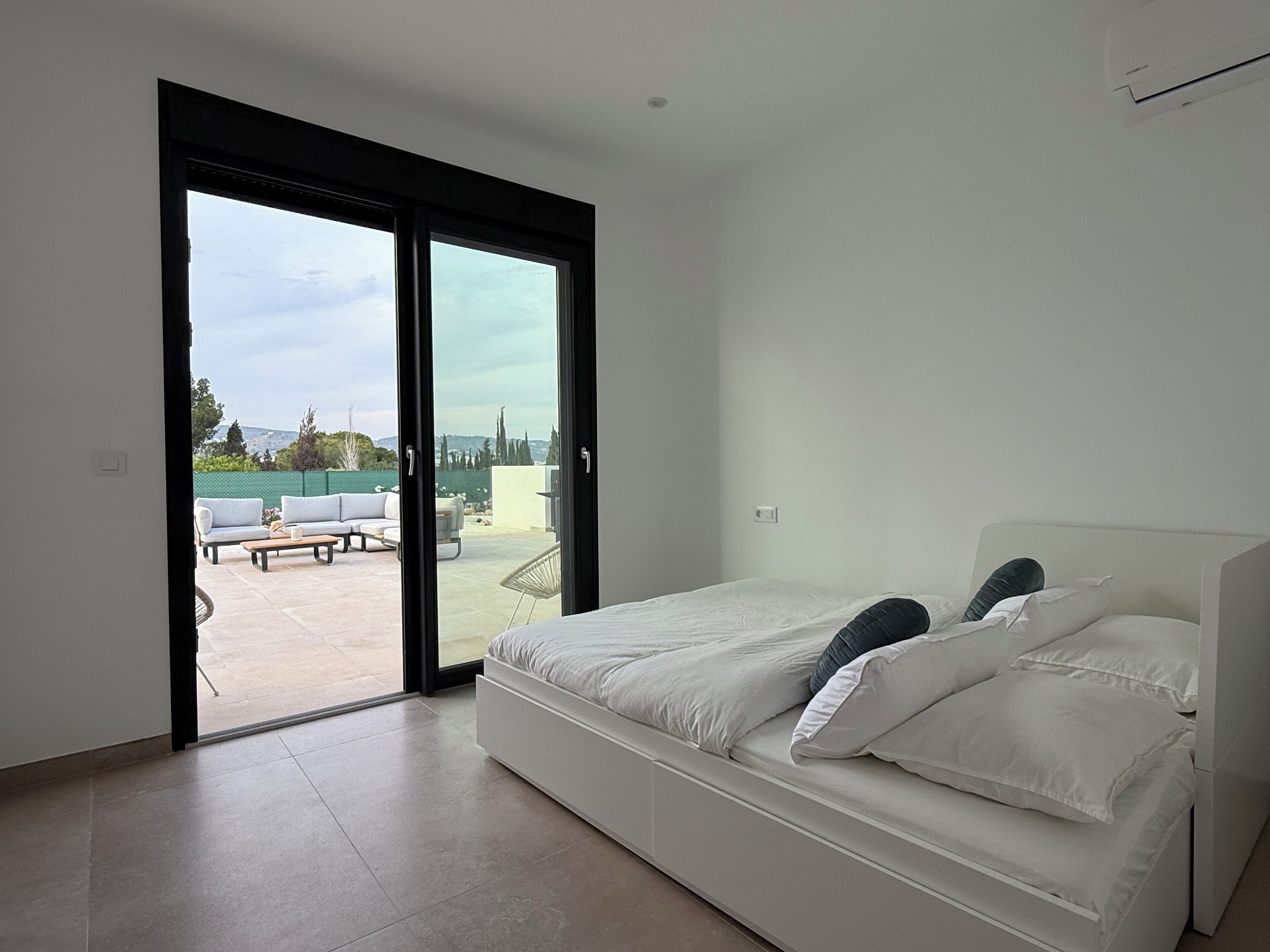 A bedroom with a bed, a sliding glass door leading to an outdoor patio with a table and chairs.