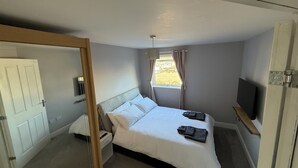 A bedroom with a bed, a nightstand, a TV mounted on the wall, and a window with curtains. - Stylish Marina Apartment with Stunning Views (Portishead)