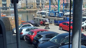 A parking area with several cars, a dock with boats, and buildings in the background. - Stylish Marina Apartment with Stunning Views (Portishead)